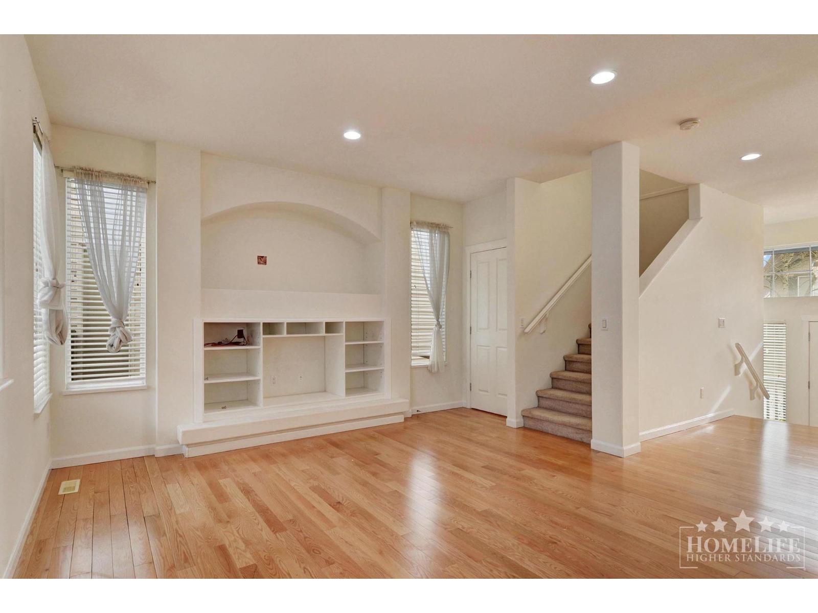 A spacious living room with wooden floors and a staircase.