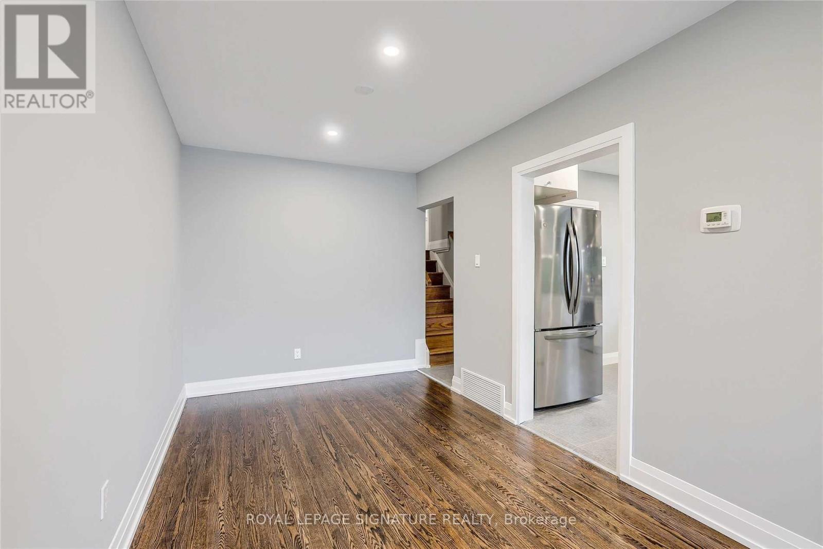 A spacious room with wooden floors and a refrigerator in the corner.