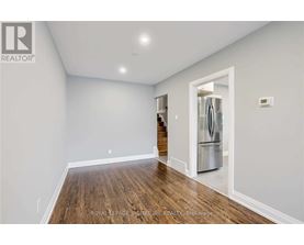 A spacious room with wooden floors and a refrigerator in the corner.
