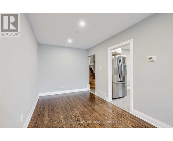 A spacious room with wooden floors and a refrigerator in the corner.