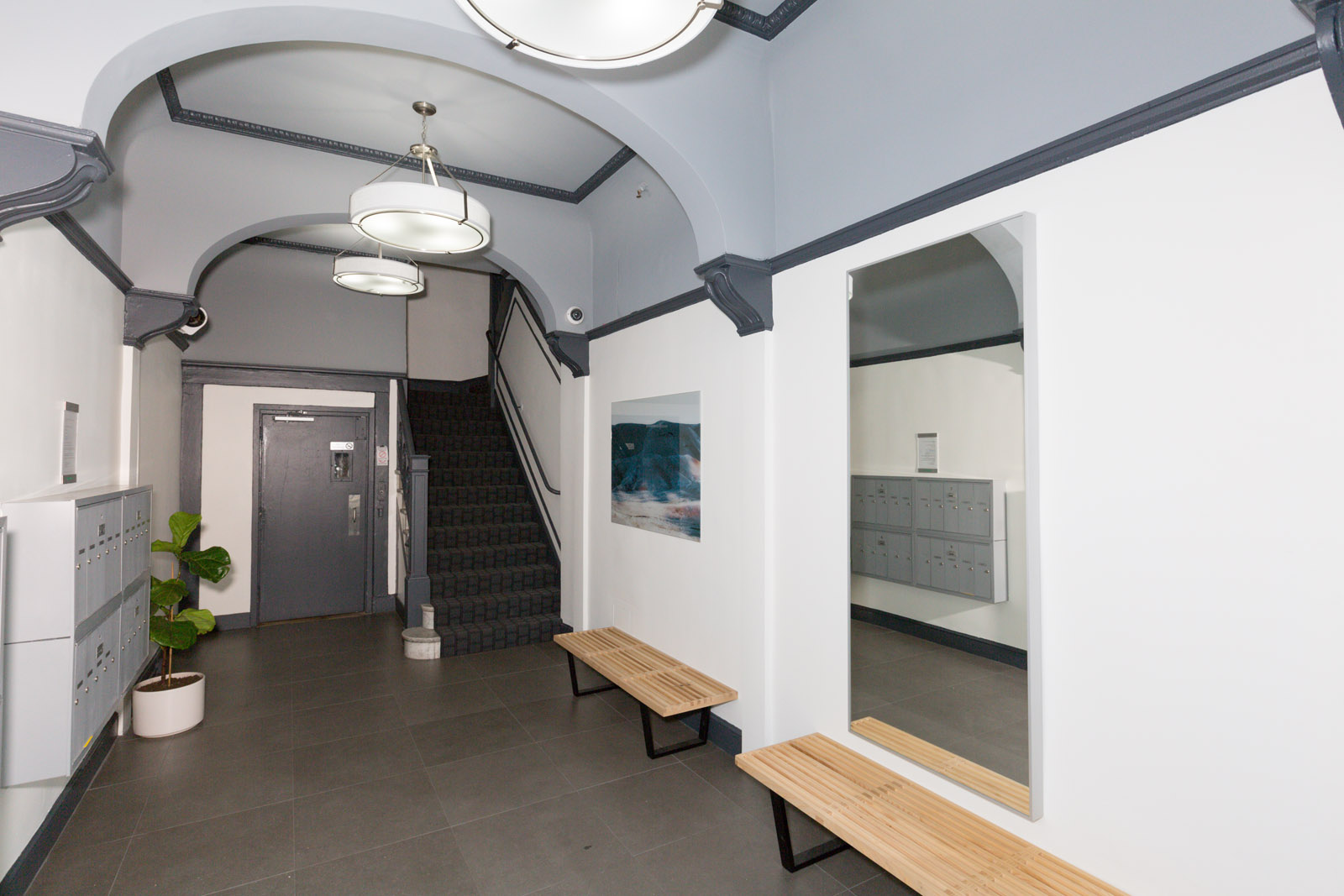 A hallway with a staircase, a plant, and a framed picture on the wall.