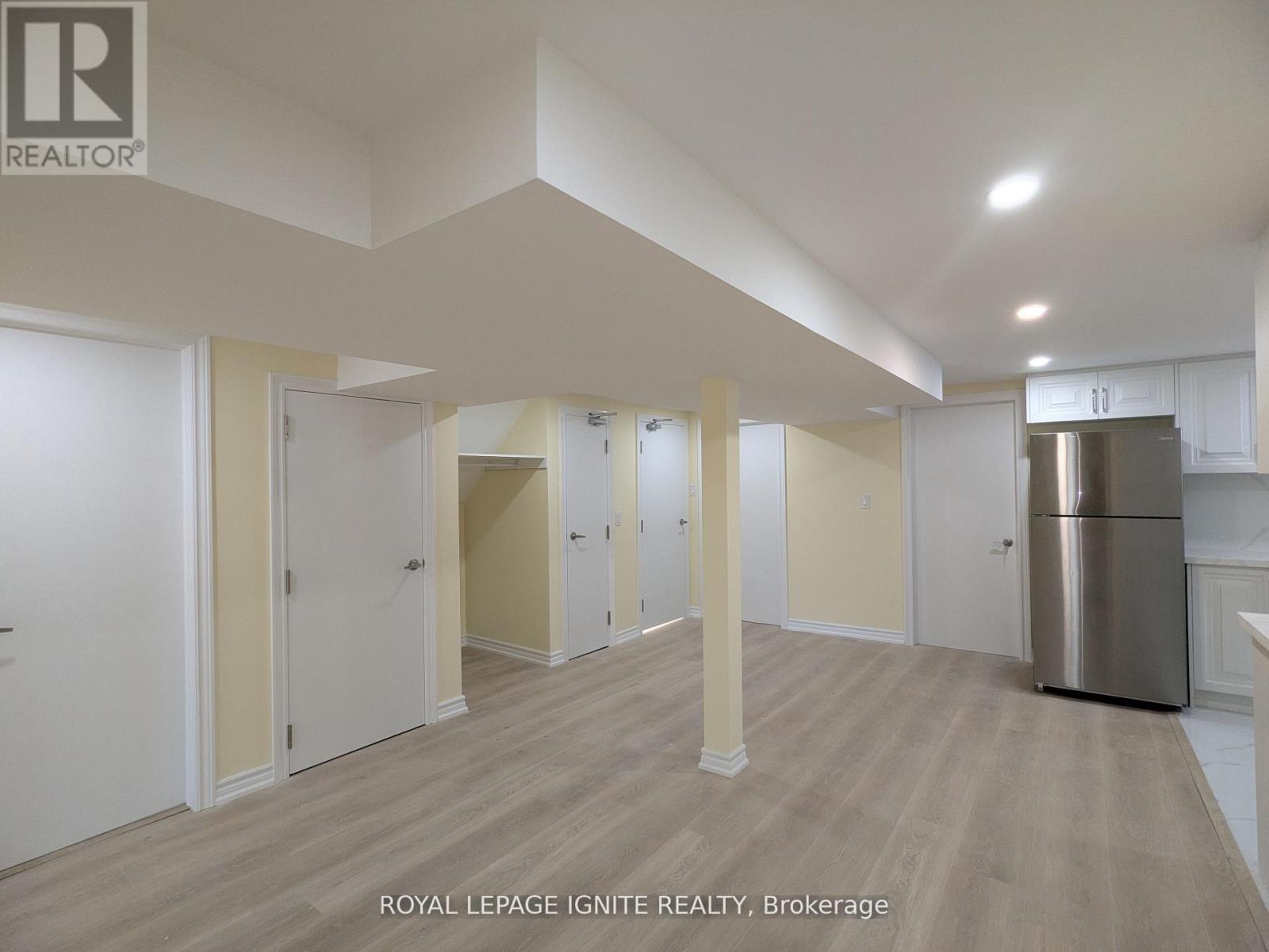 A spacious room with wooden flooring and white walls, with a stainless steel refrigerator on the right side.