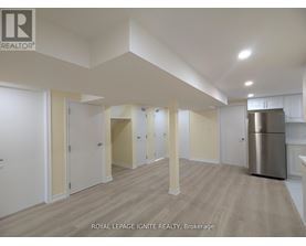 A spacious room with wooden flooring and white walls, with a stainless steel refrigerator on the right side.