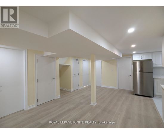 A spacious room with wooden flooring and white walls, with a stainless steel refrigerator on the right side.