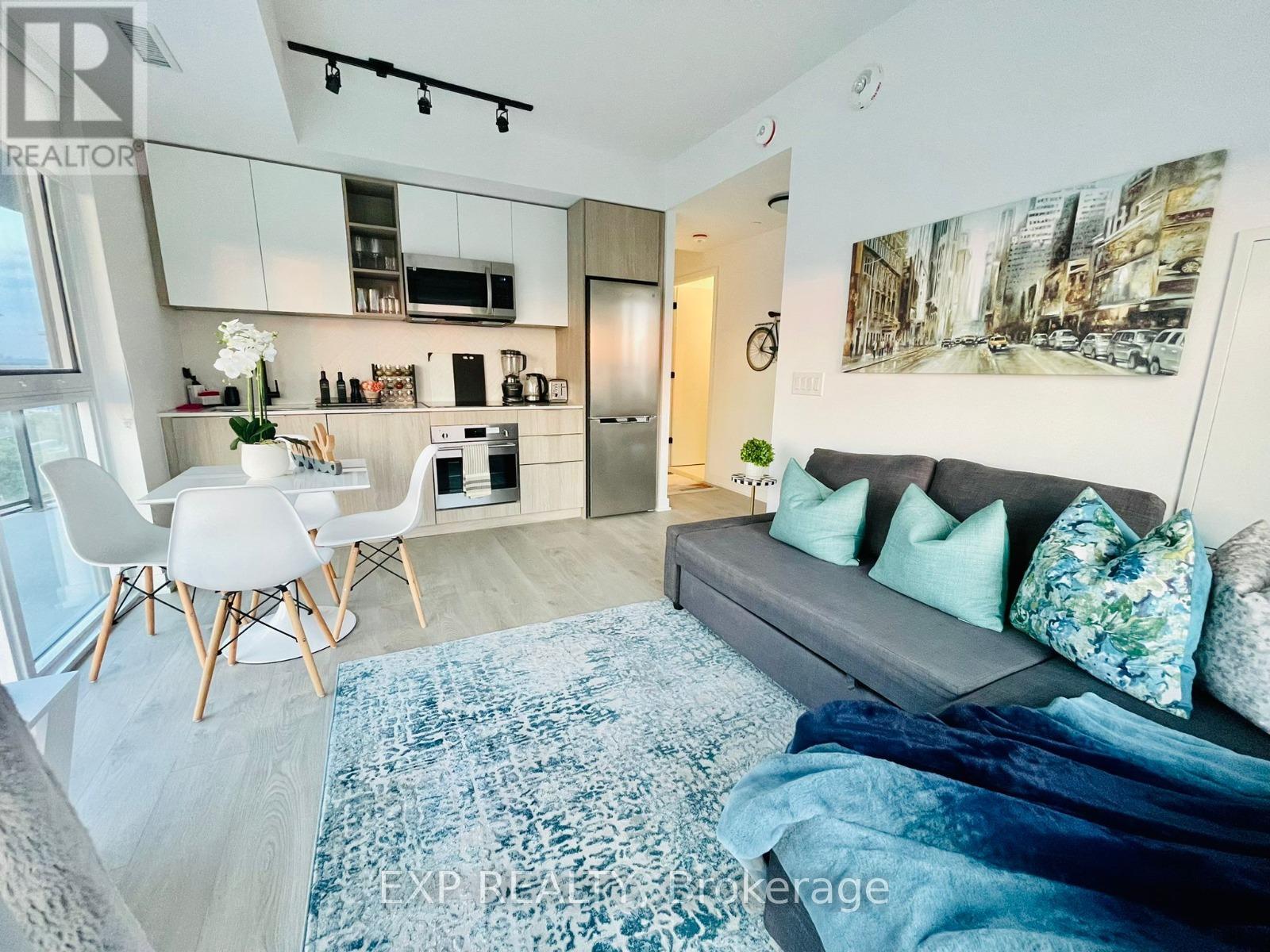 A modern living room with a grey couch and a kitchen area in the background.