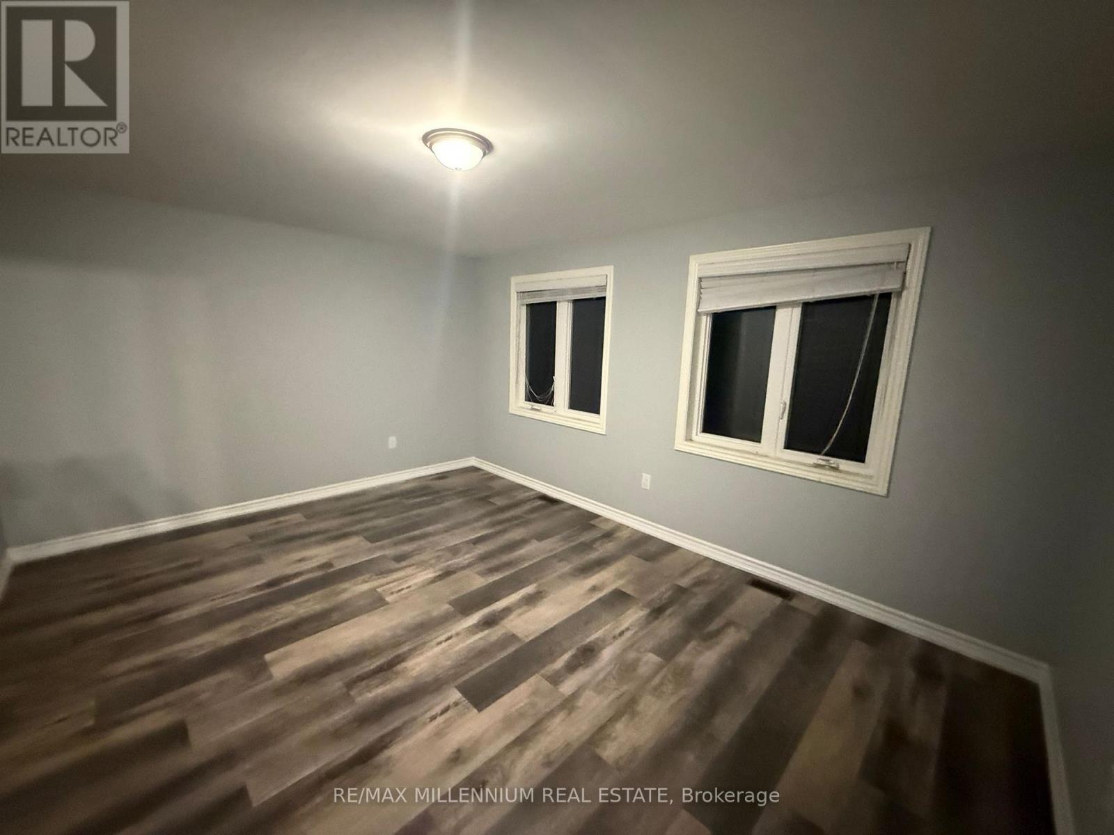 A room with wooden flooring and two windows.