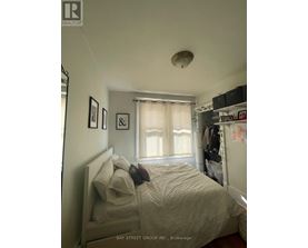 A bedroom with a bed, a window with curtains, and a shelf with various items.