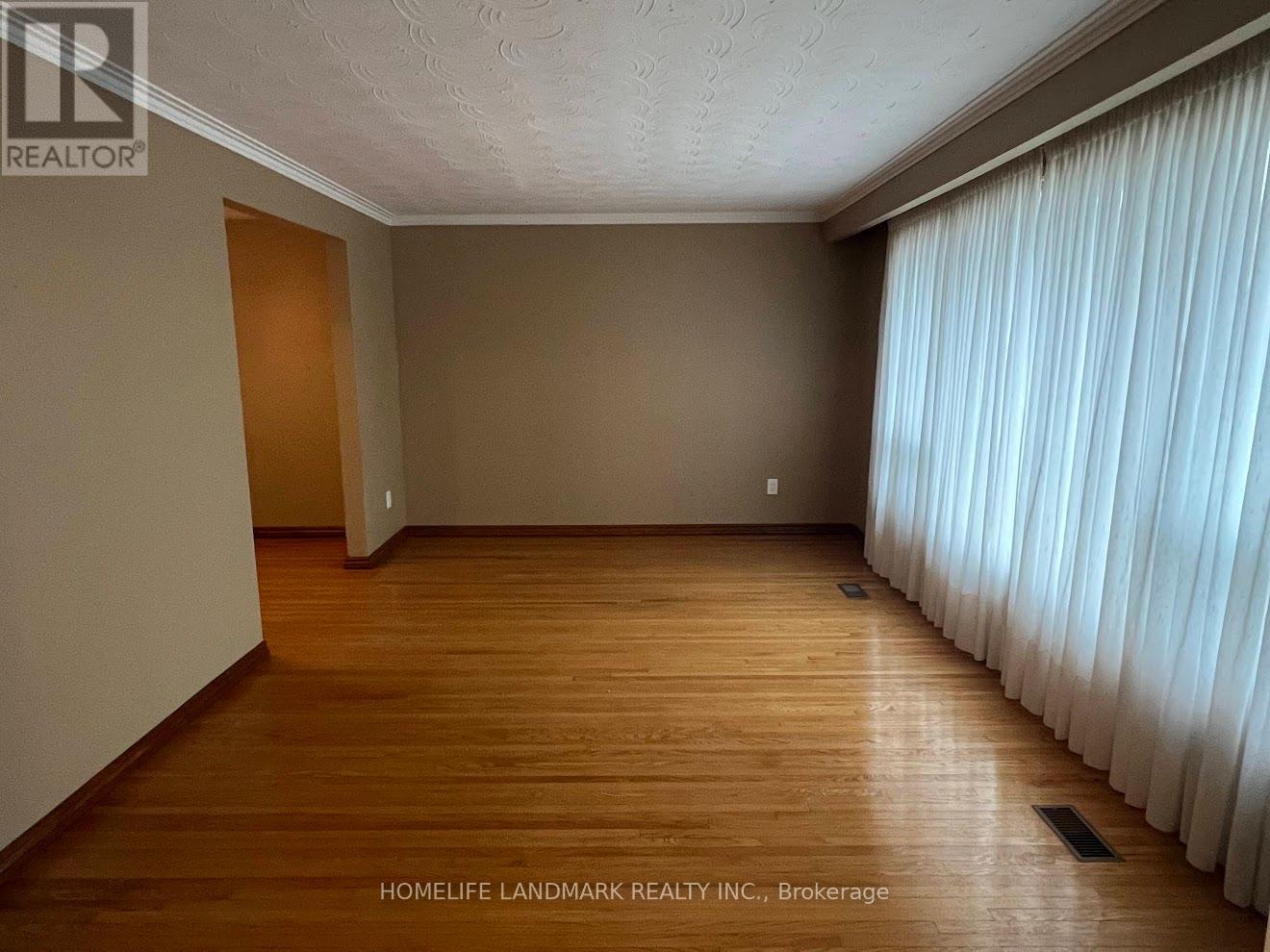 A room with wooden flooring and a window with white curtains.