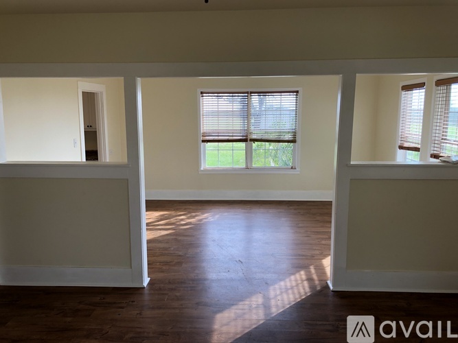 A room with wooden floors and three windows with blinds.