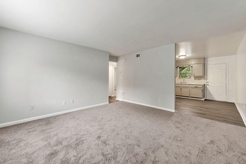 an empty living room with a kitchen in the background
