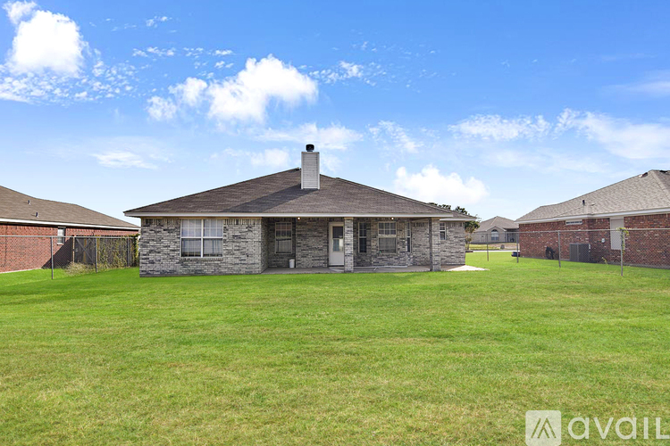 A house with a stone facade and a brown roof is surrounded by a grassy field.