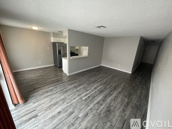 A spacious room with grey flooring and a kitchen area in the background.