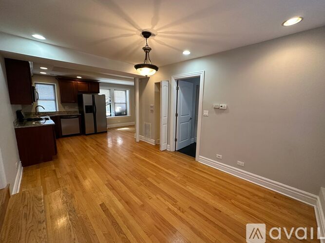A well-lit room with wooden floors and a kitchen area with a refrigerator, sink, and cabinets.
