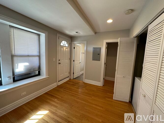 A room with wooden floors and white walls, featuring a window with blinds, a door, and a closet.