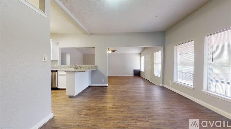 A spacious room with wooden floors and a kitchen area in the background.