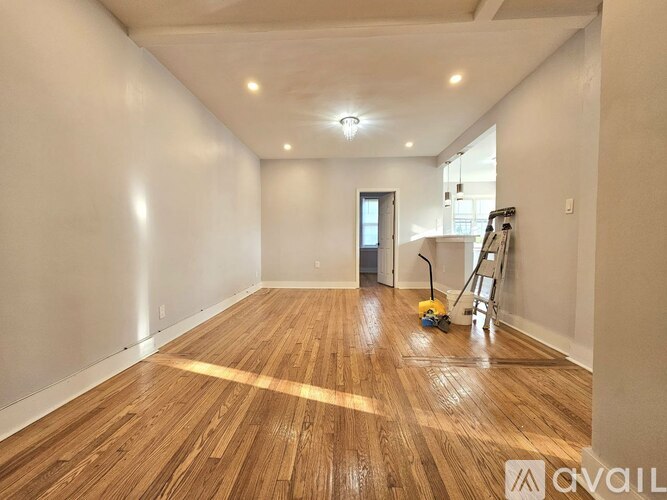 A room with wooden flooring and white walls, with a ladder and vacuum cleaner on the floor.