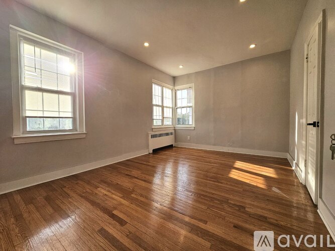 A room with wooden flooring and two windows.
