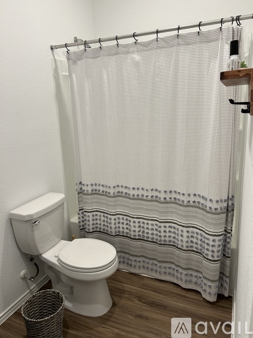A white toilet sits next to a white shower curtain in a bathroom.