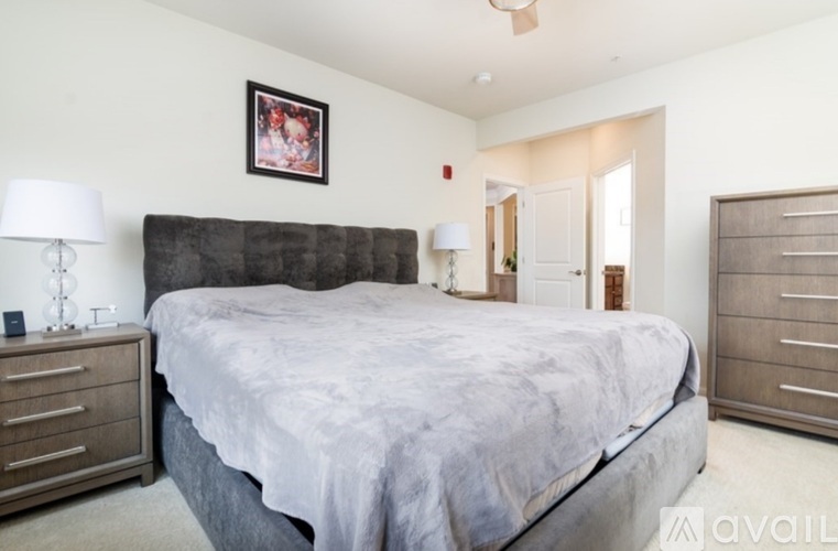 A bedroom with a large bed, a nightstand with a lamp, and a framed picture on the wall.