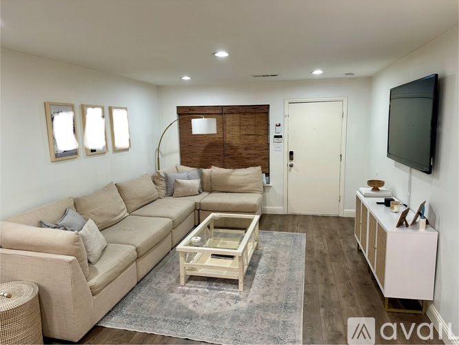 A living room with a beige sofa, a wooden coffee table, and a flat-screen TV mounted on the wall.