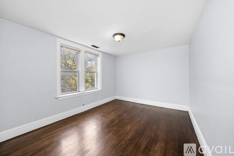 A room with wooden floors and a window showing trees outside.