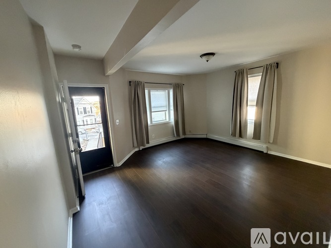 A spacious room with wooden floors and a large window with curtains.