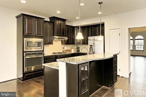 A kitchen with black cabinets and a marble island.