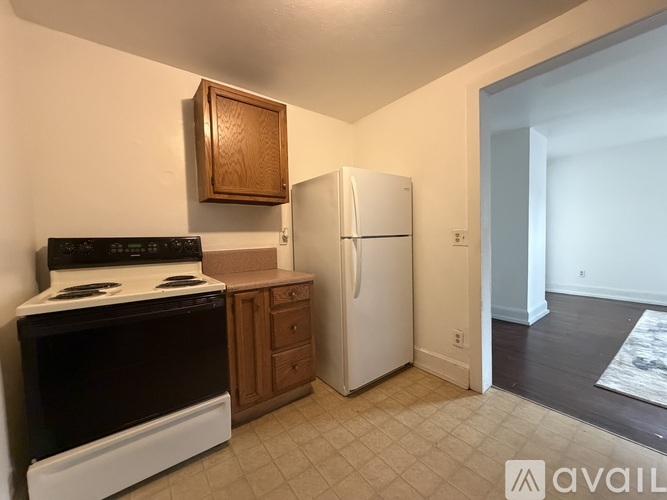 A kitchen with a black stove top oven, a white refrigerator, and a wooden cabinet.