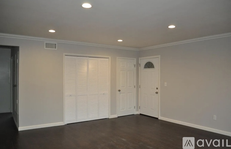 A room with a dark floor and white walls, with a door on the right and a window with blinds on the left.