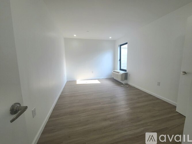 A room with wooden flooring and a window letting in sunlight.