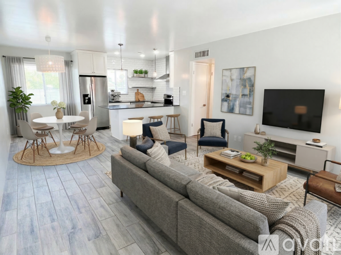 A modern living room with a grey sofa, a round table with four chairs, and a television on the wall.