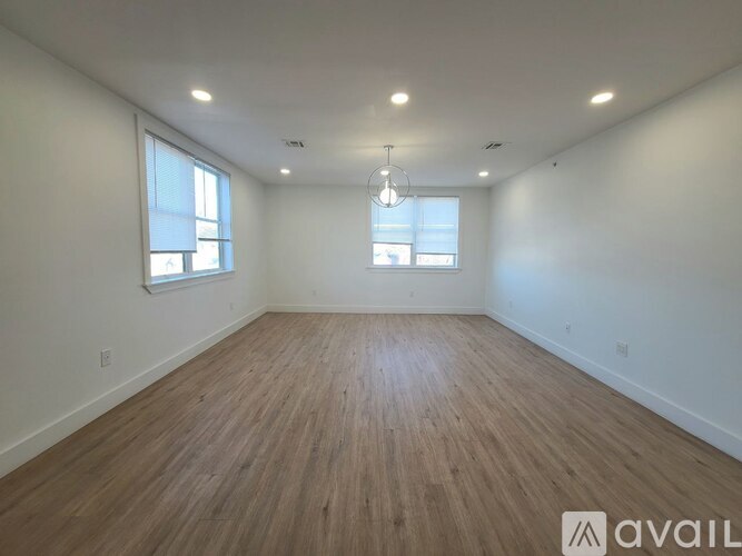 A spacious room with wooden flooring and two windows.