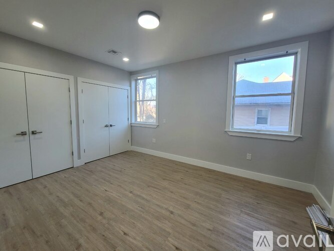 A room with wooden flooring and a window showing a view of a house.