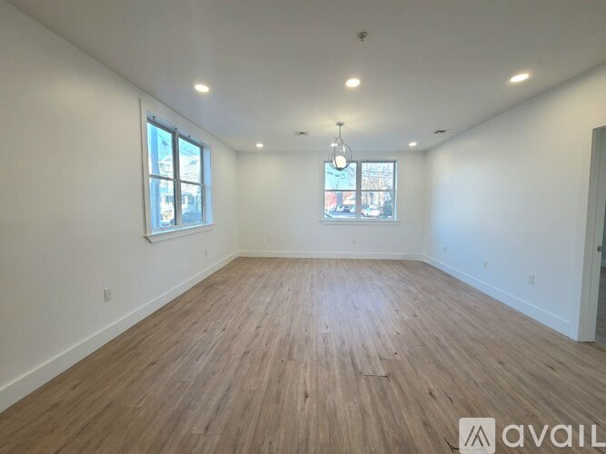 A room with wooden flooring and two windows.