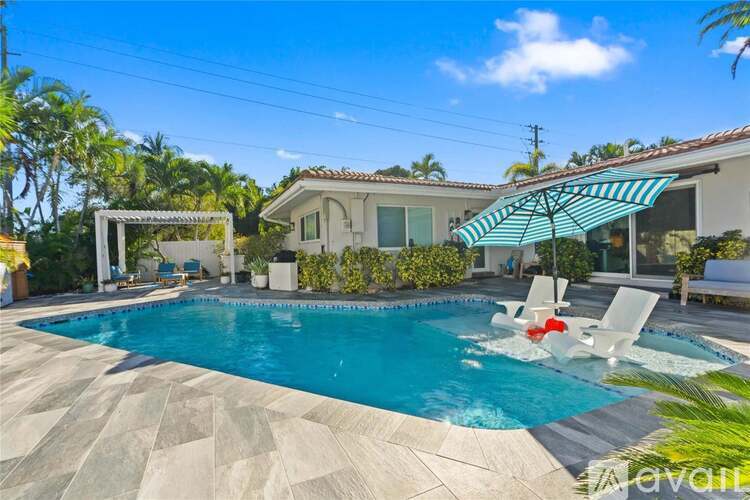 A pool with a white umbrella and a house in the background.