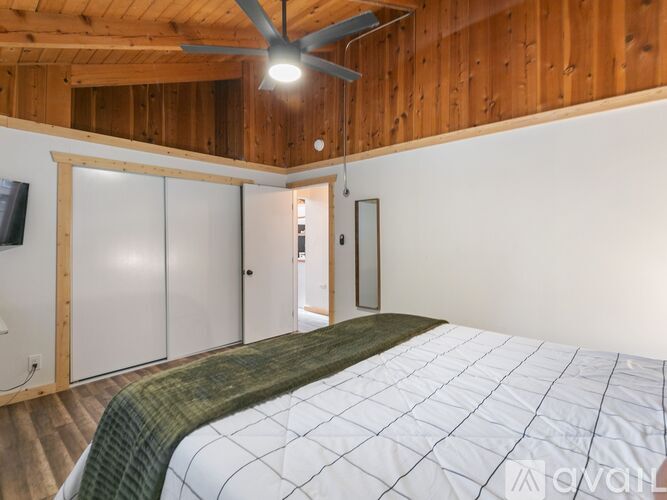 A bedroom with a bed, a ceiling fan, and a door leading to another room.