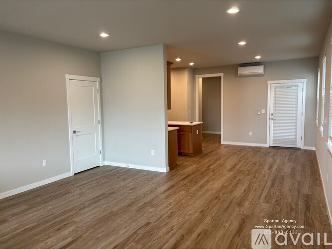 A room with wooden flooring and white walls, with a door on the left and a window on the right.