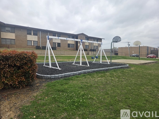 A playground with swings and a basketball hoop in front of a brick building.