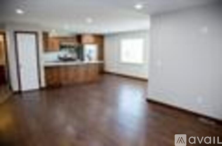 A spacious room with wooden flooring and a kitchen area in the background.