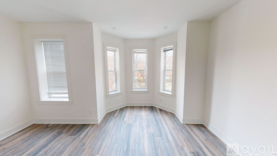 A room with wooden flooring and three windows.