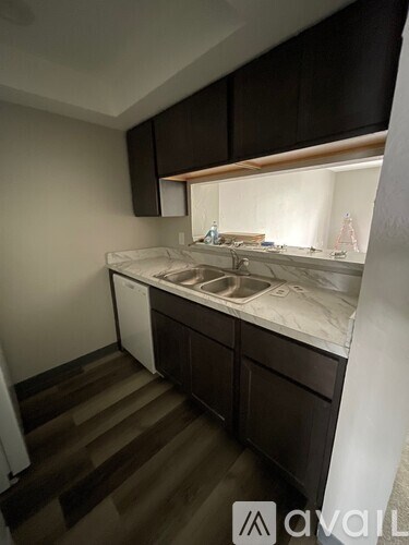 A small, dark brown kitchen with a white dishwasher and a white sink.