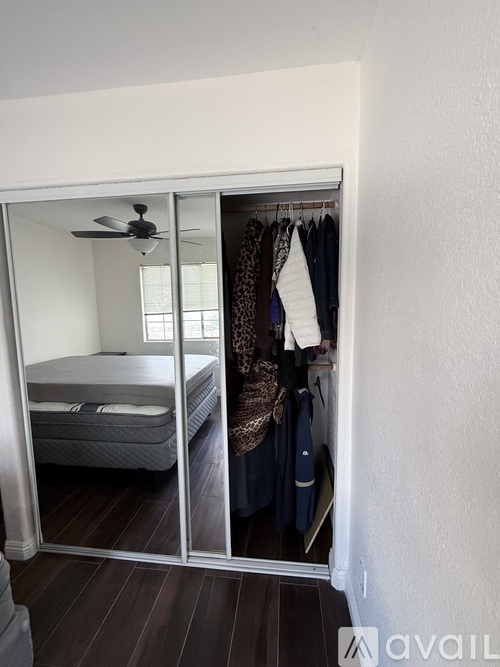 A bedroom with a bed, a fan, and a wardrobe with clothes hanging on it.