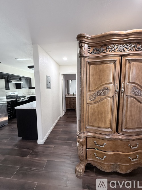 A large wooden armoire with ornate carvings stands in a room with dark wood flooring.