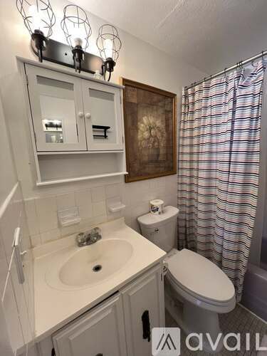 A bathroom with a sink, toilet, and a cabinet with lights above it.