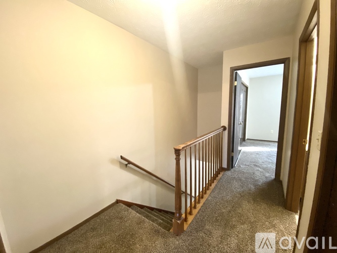 A hallway with a carpeted floor and a wooden staircase.