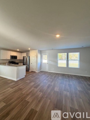 A spacious room with wooden flooring and a kitchen area with white cabinets and appliances.