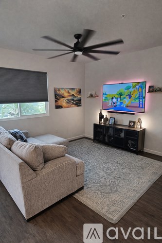 A living room with a beige couch, a ceiling fan, and a television displaying a cartoon.
