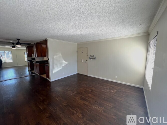 A room with wooden floors and white walls, with a ceiling fan and a door leading to another room.
