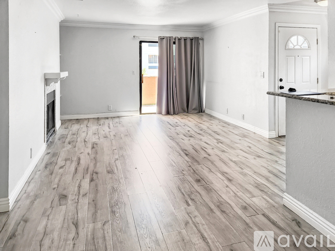 A spacious room with wooden flooring and a fireplace on the left side.