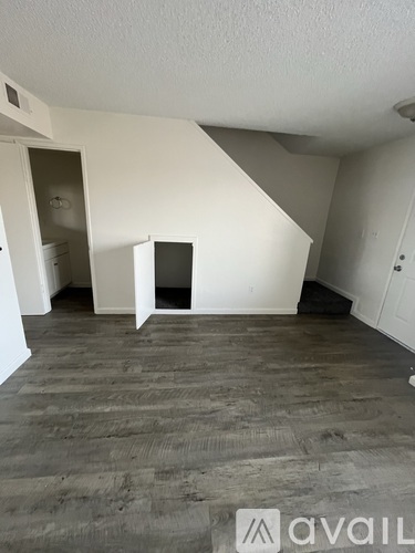 A room with wooden flooring and white walls, with a doorway leading to another room.